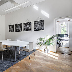 Modernes Besprechungszimmer von Kling Consult am Standort Augsburg mit einem langen weissen Tisch, Stühlen, Kunstwerken an der Wand, einer Zimmerpflanze und Parkettboden