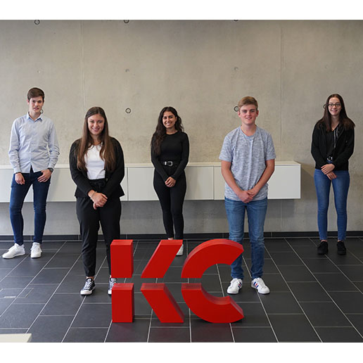 Gruppenfoto der fünf Auszubildenden 2020 von Kling Consult vor einer Betonwand und dem KC Logo vor Ihnen