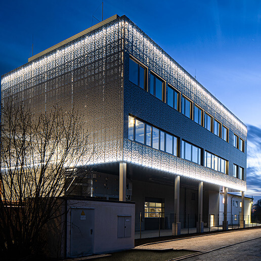 Modernes Bürogebäude bei Dämmerung beleuchtet, mit reflektierender Fassade der Chemische Fabrik Karl Bucher 