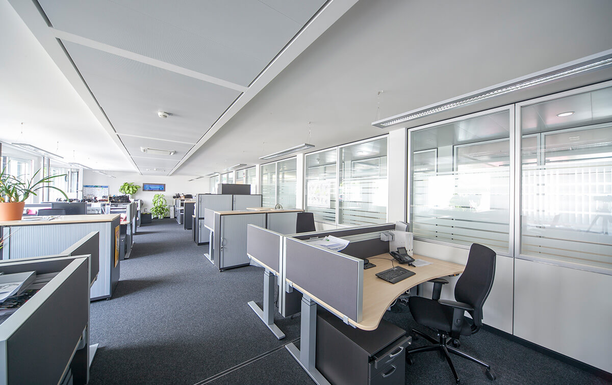 Moderne Innenansicht Bürogebäude O3/O4 mit Reihen von Schreibtischen, Bürostühlen und Computern, getrennt durch transparente Trennwände, mit heller Beleuchtung