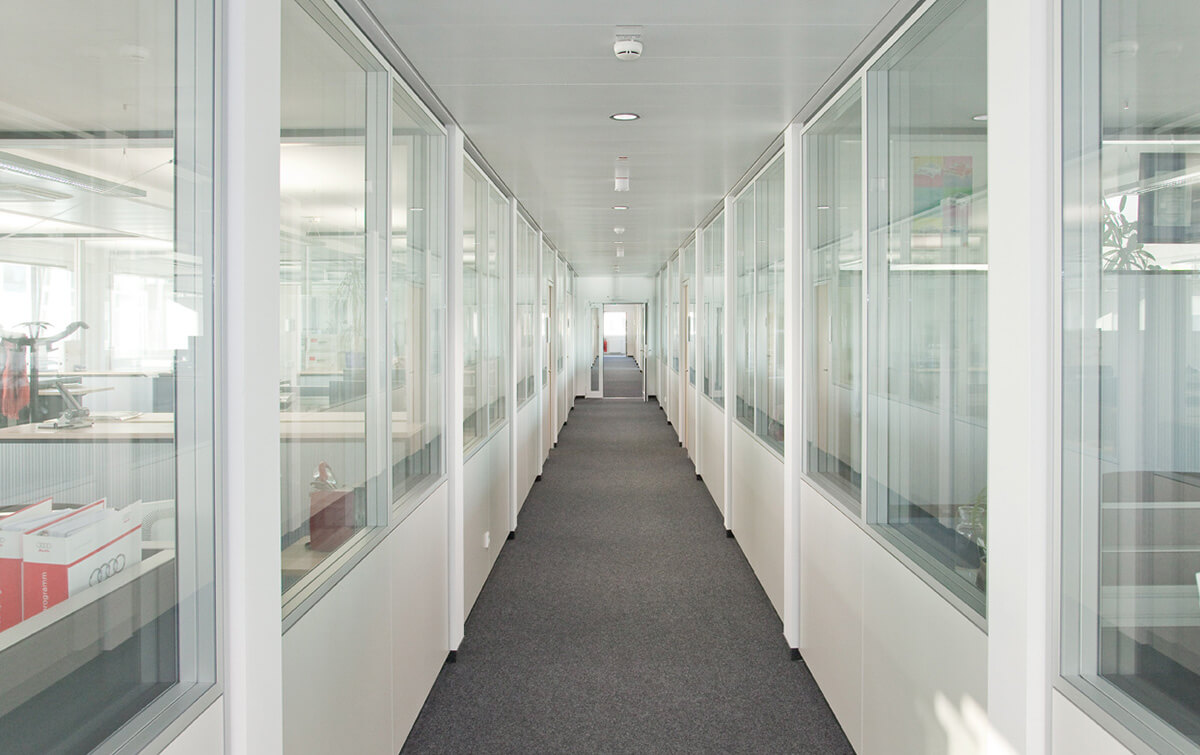 Innenansicht Bürogebäude S50 - langer, heller Flur in einem Bürogebäude mit gläsernen Besprechungsräumen auf beiden Seiten und einem dunklen Teppichboden