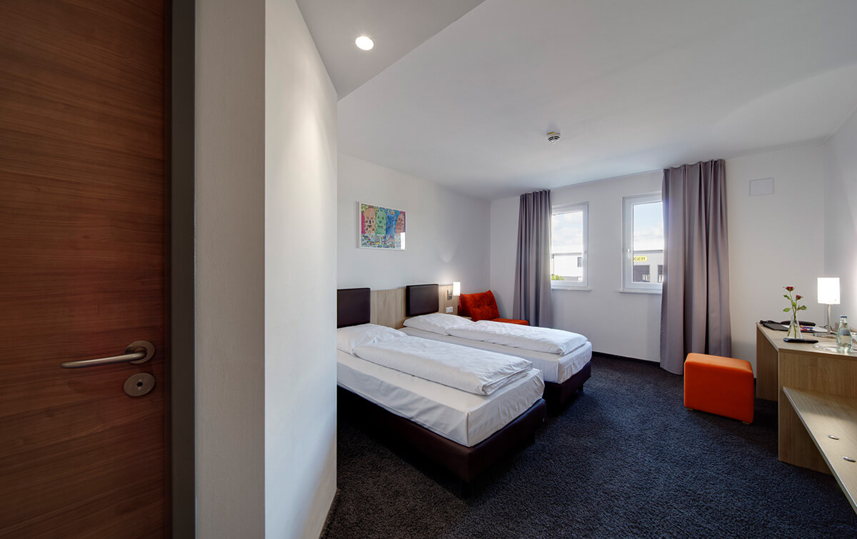 Hotelzimmer im Eurohotel Derching-West mit einem Doppelbett, Nachttischen, Kunst an der Wand, einem Schreibtisch und einem Sitzbereich, natürlich beleuchtet durch Fenster mit Vorhängen 