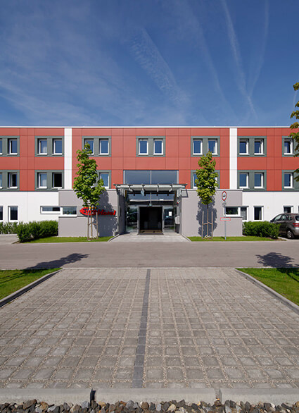Eingangsbereich des Eurohotels Derching-West mit symmetrischen Fenstern, zentralem Eingang und zwei Bäumen an der Front